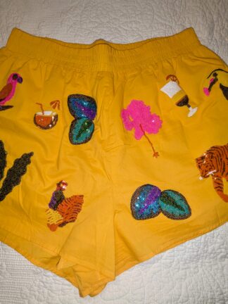 Bright yellow Queen of Sparkles running shorts with sequin tiger, parrot, and cocktail patches